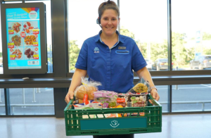 An Aldi employee holding a green crate of groceries